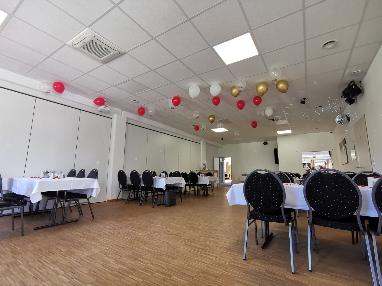 Saal links mit runden Tischen und roter Ballondekoration