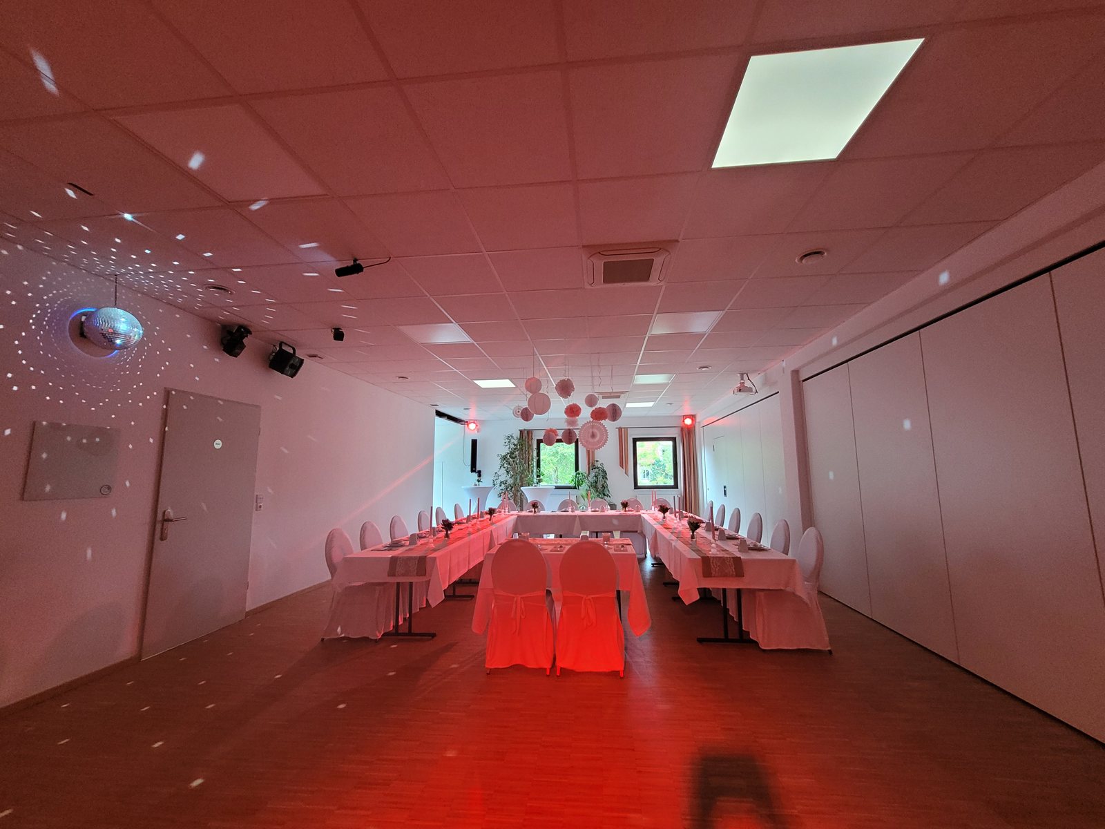 Saal links in rotem Stimmungslicht mit langer Tafel