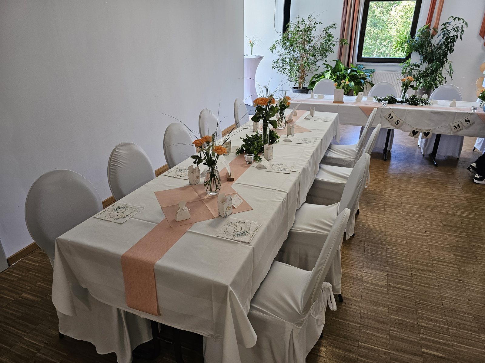 Gedeckte Tafel im Saal links mit Blumen und Tischlaeufern in Apricot