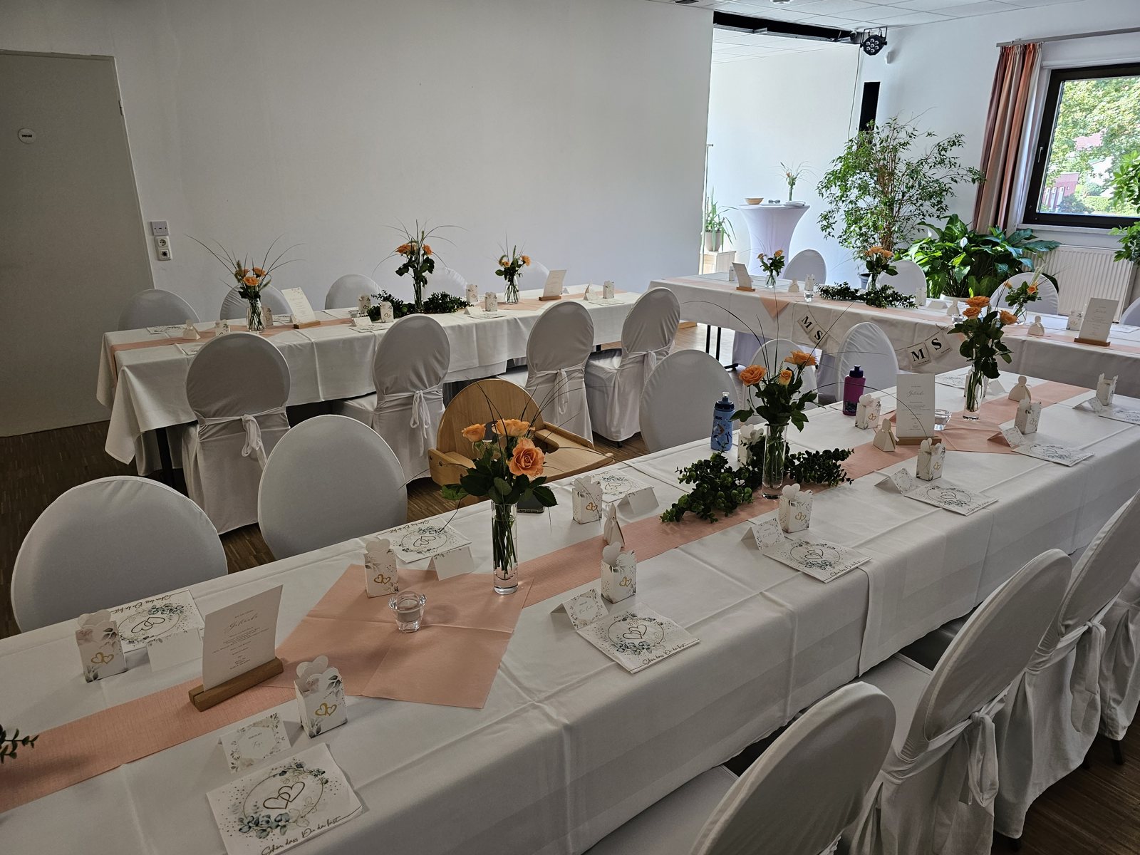 Saal links mit heller Tafel, Blumenschmuck und Tageslicht